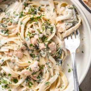 A fork scooping a creamy pasta with salmon and parsley.