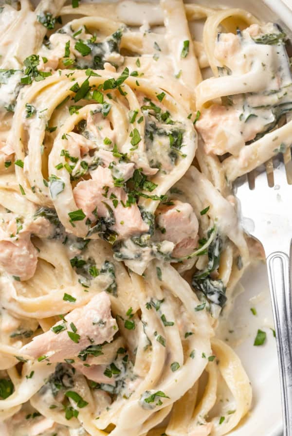 A fork scooping a creamy pasta with salmon and parsley.