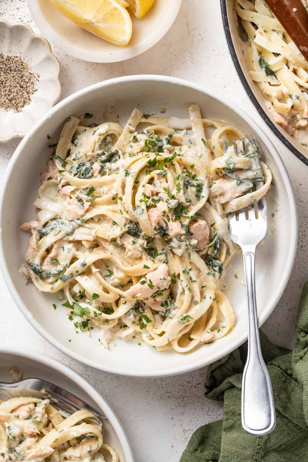A bowl of creamy pasta with salmon next to some lemon slices.