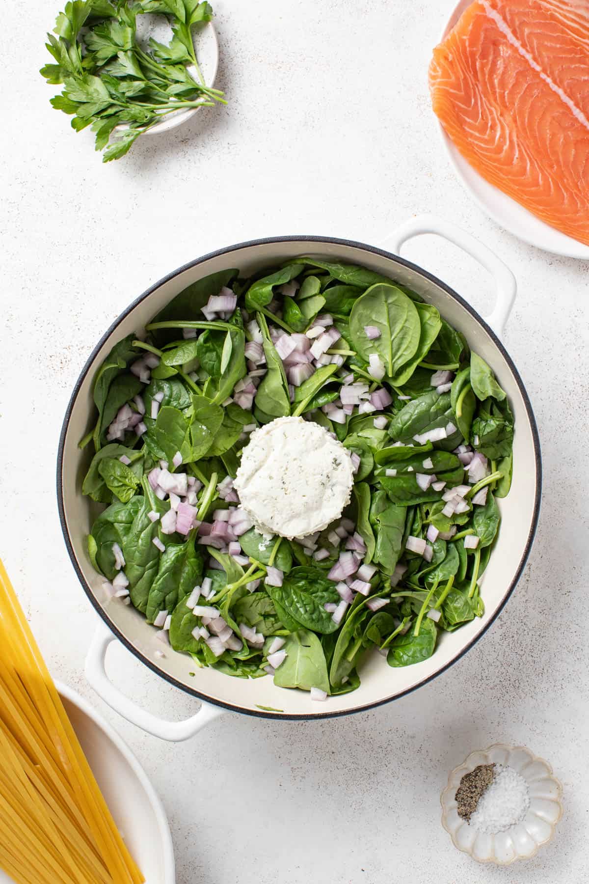 Boursin cheese in the center of a baking dish with shallots and spinach.