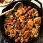 Chicken thighs in a cast iron skillet with grapes, shallots, and rosemary.