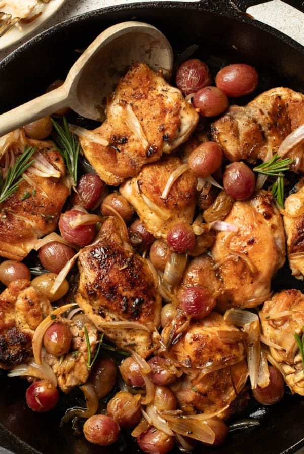 Chicken thighs in a cast iron skillet with grapes, shallots, and rosemary.