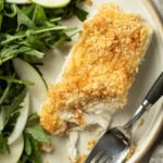 A plate with baked halibut and a panko topping next to a salad.