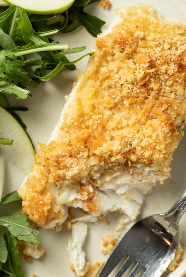 A plate with baked halibut and a panko topping next to a salad.