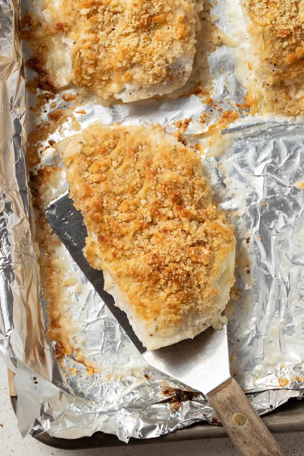 Scooping the baked halibut with mayonnaise and panko off the sheet pan.