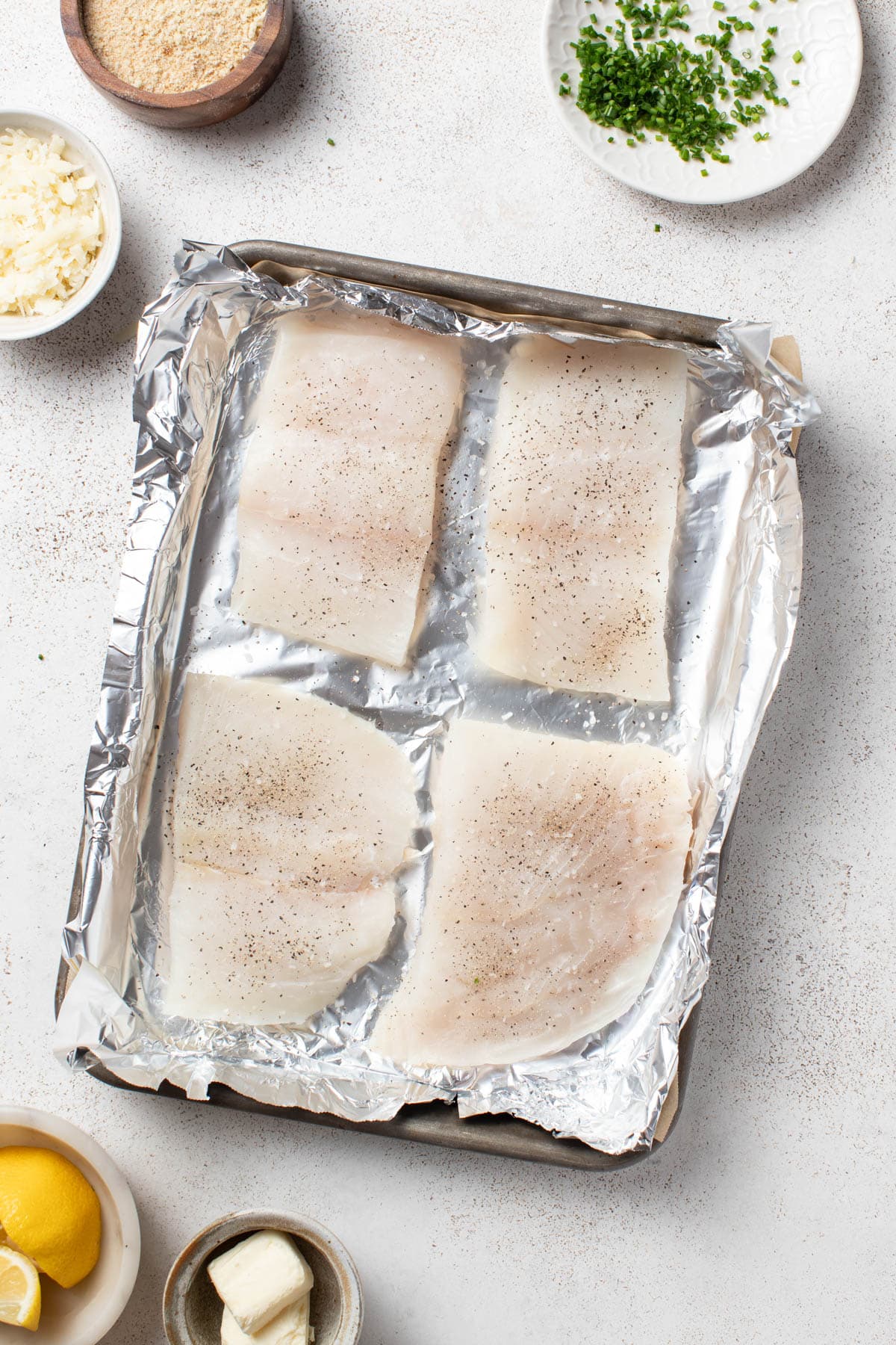 Seasoning the halibut with salt and pepper on a sheet pan.