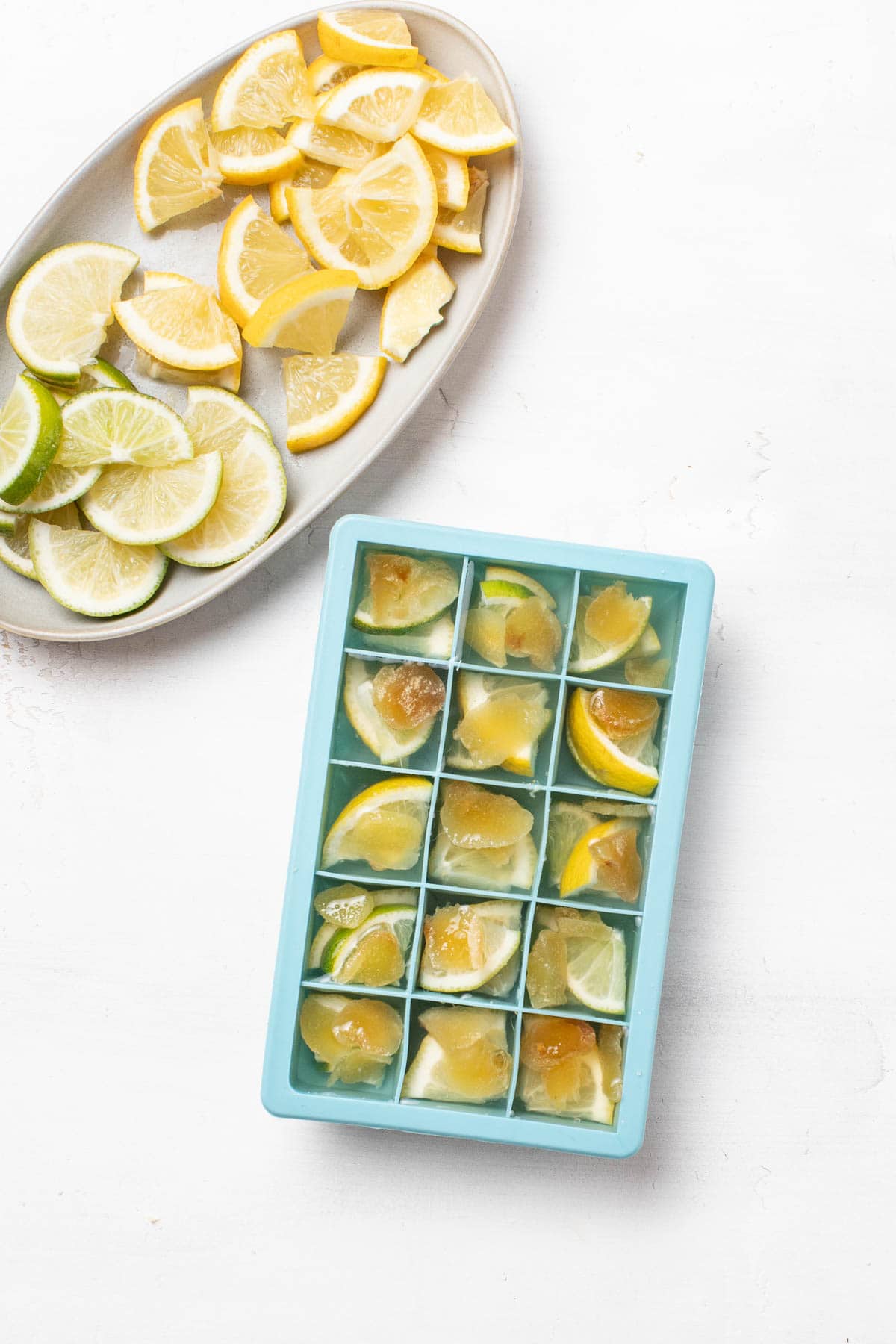 Lemons, ginger, and limes being added to a bowl.