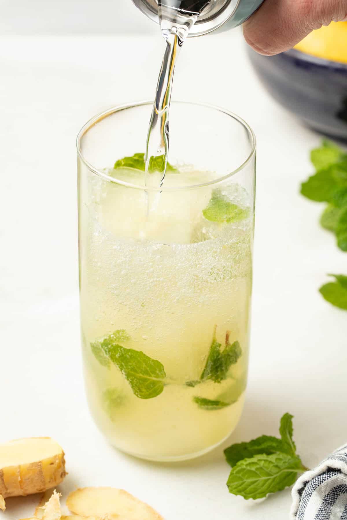 Pouring ginger beer into the glass with lemon and mint. 