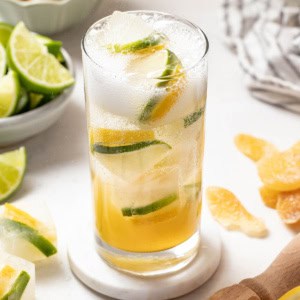 Homemade sprite with lemon lime ice cubes in a tall glass with fresh lemons and limes in the background.