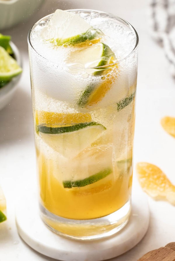 Homemade sprite with lemon lime ice cubes in a tall glass with fresh lemons and limes in the background.