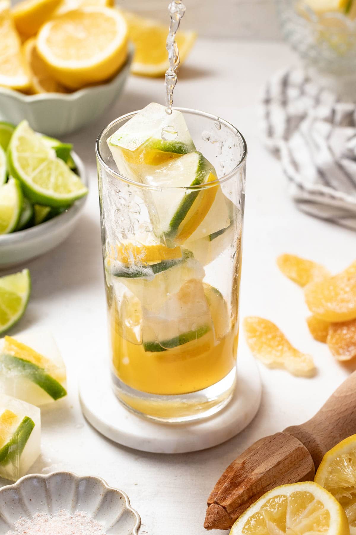 Lemon lime ice cubes and citrus mixture being combined in a tall glass.