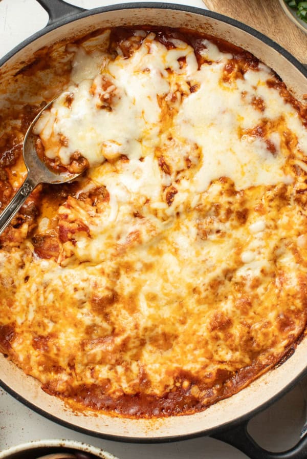 A spoon scooping out a cheesy beef enchilada casserole.