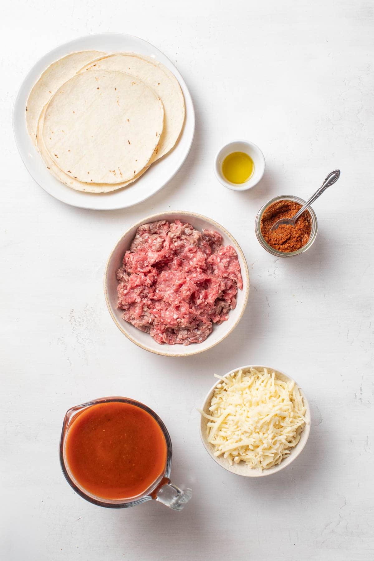 Ingredients for lazy enchiladas including ground beef, tortillas, enchilada sauce and cheese.