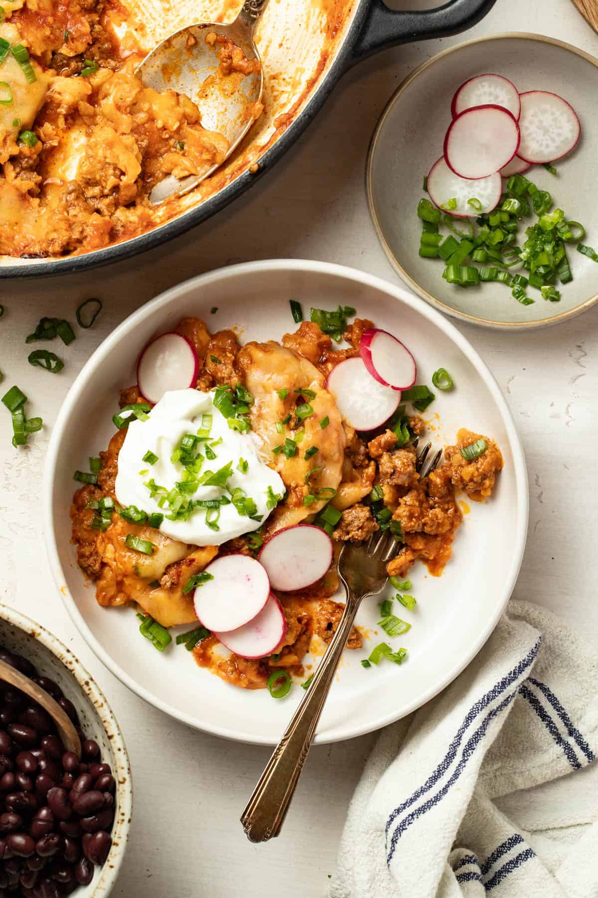 Lazy enchilada casserole topped with sour cream and sliced radish.
