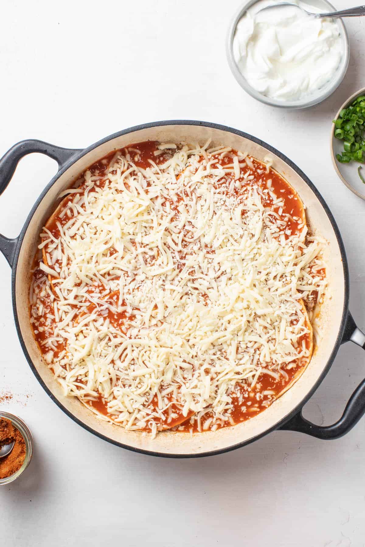 Putting cheese on top of the enchiladas.