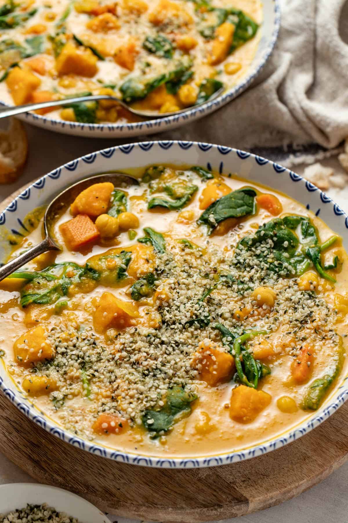 Two bowls of vegetable stew topped with hemp seeds next to a napkin with bread.