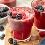 A mixed berry mocktail on a wood cutting board with fresh mixed berries on top.