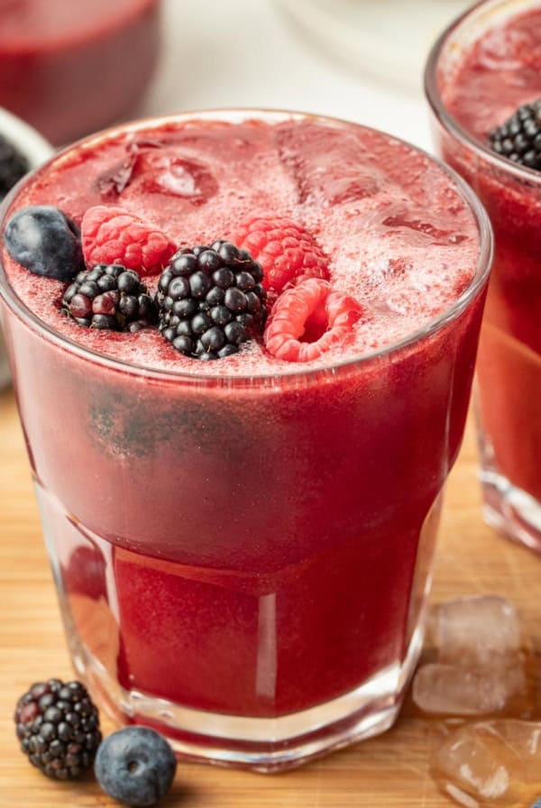 A mixed berry mocktail on a wood cutting board with fresh mixed berries on top.