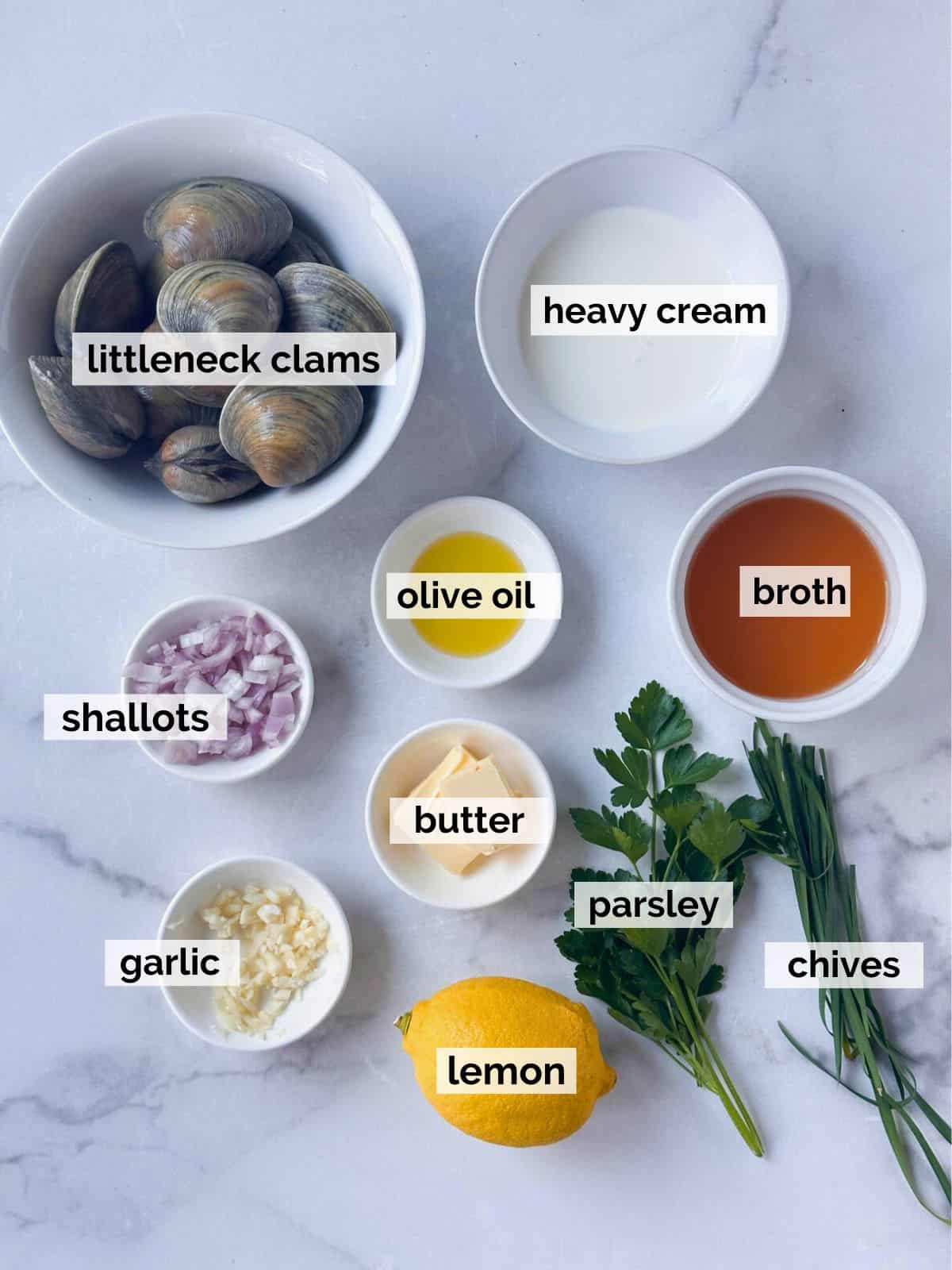 Ingredients for steamed littleneck clams on a white table.