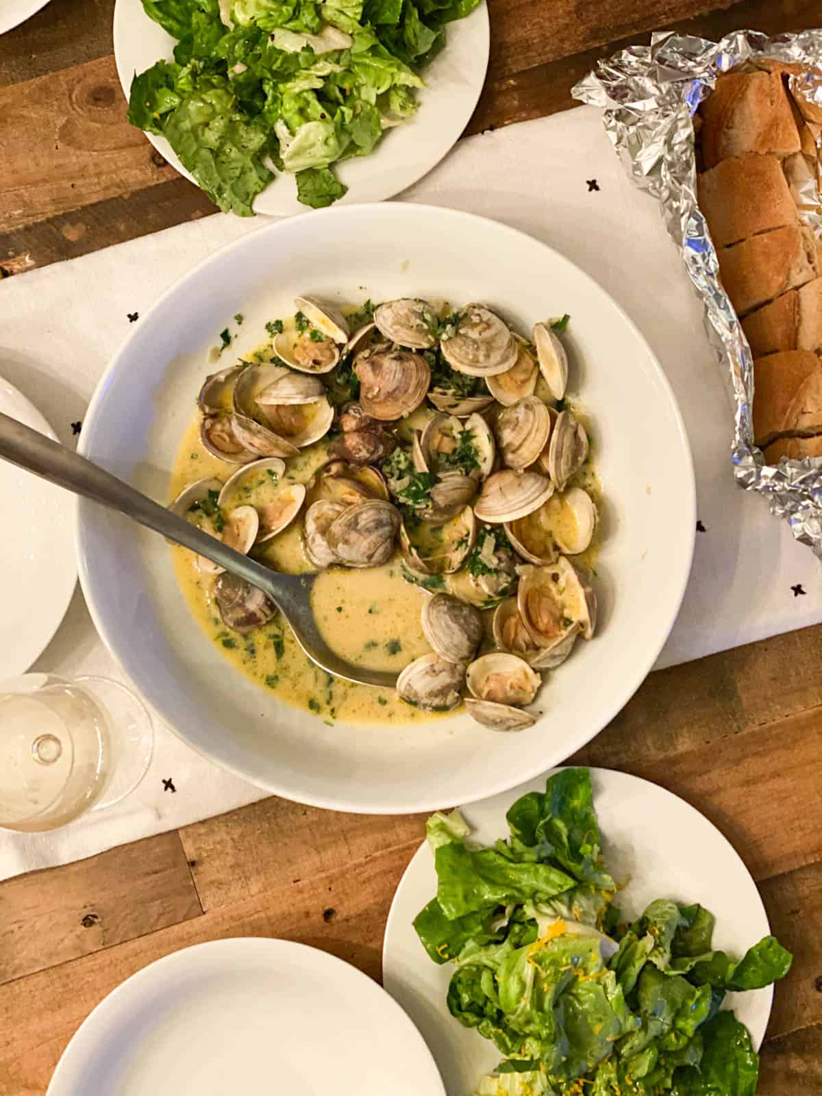 A bowl of steamed clams next to two green salads and warm crusty bread.
