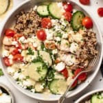 A chicken quinoa bowl with tomatoes, cucumber, and feta and a Mediterranean dressing drizzled on top.