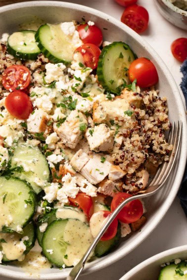 A big bowl of quinoa and chicken with Mediterranean toppings and a fork to the side.