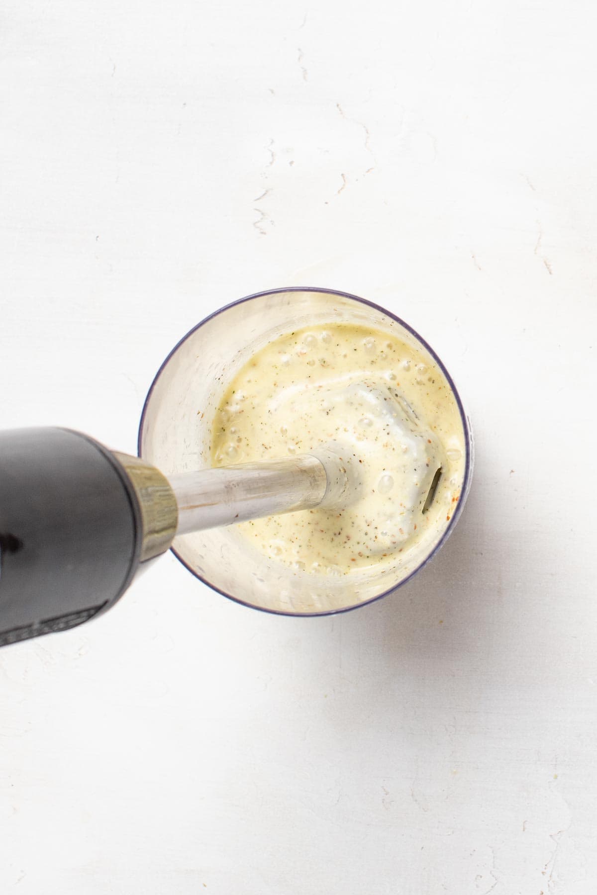 Blending olive oil and spices together with an immersion blender in a tall glass to create the vinaigrette.