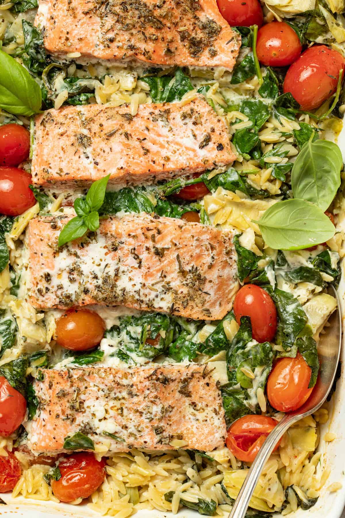 Salmon fillets in a baking dish with creamy orzo, spinach, and cherry tomatoes.