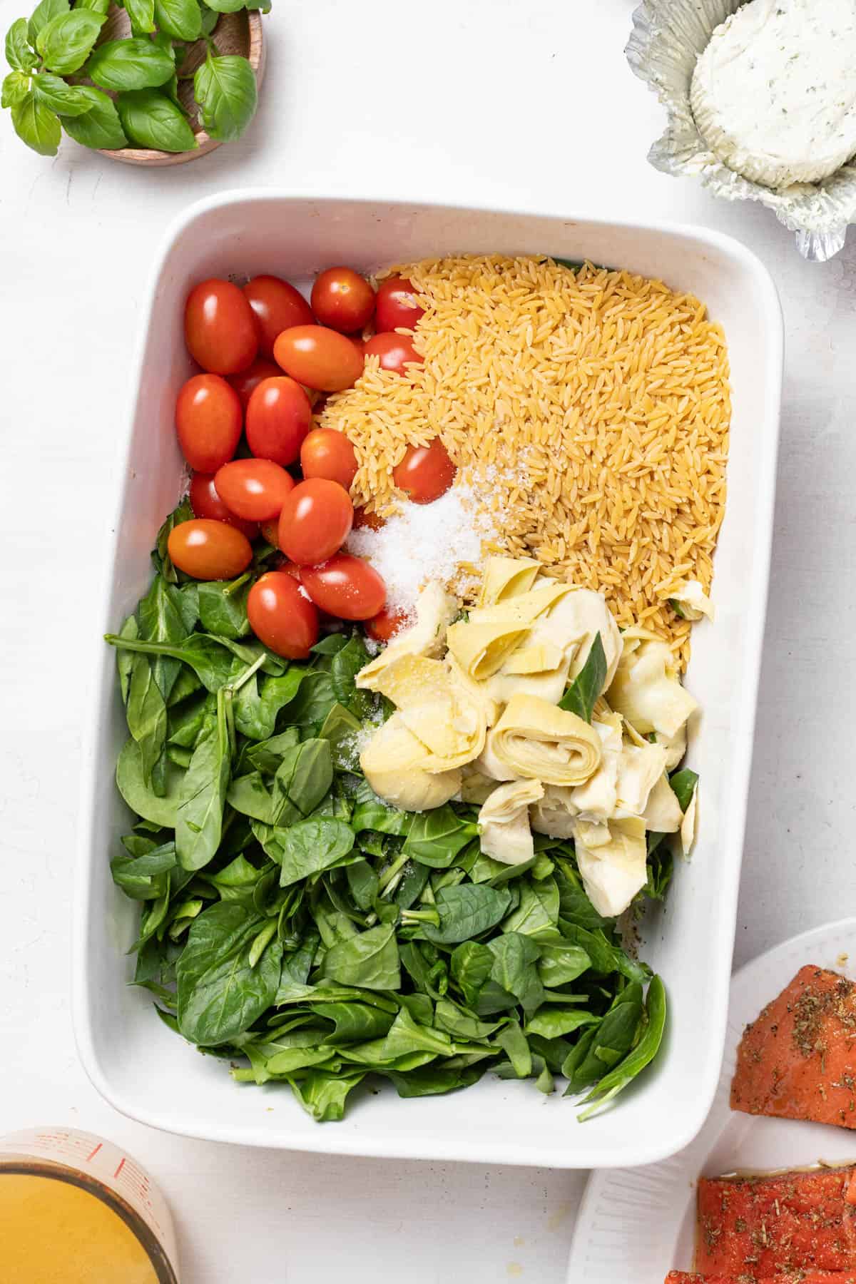 Orzo, tomatoes, spinach, artichokes, seasoning, and broth in a baking dish.