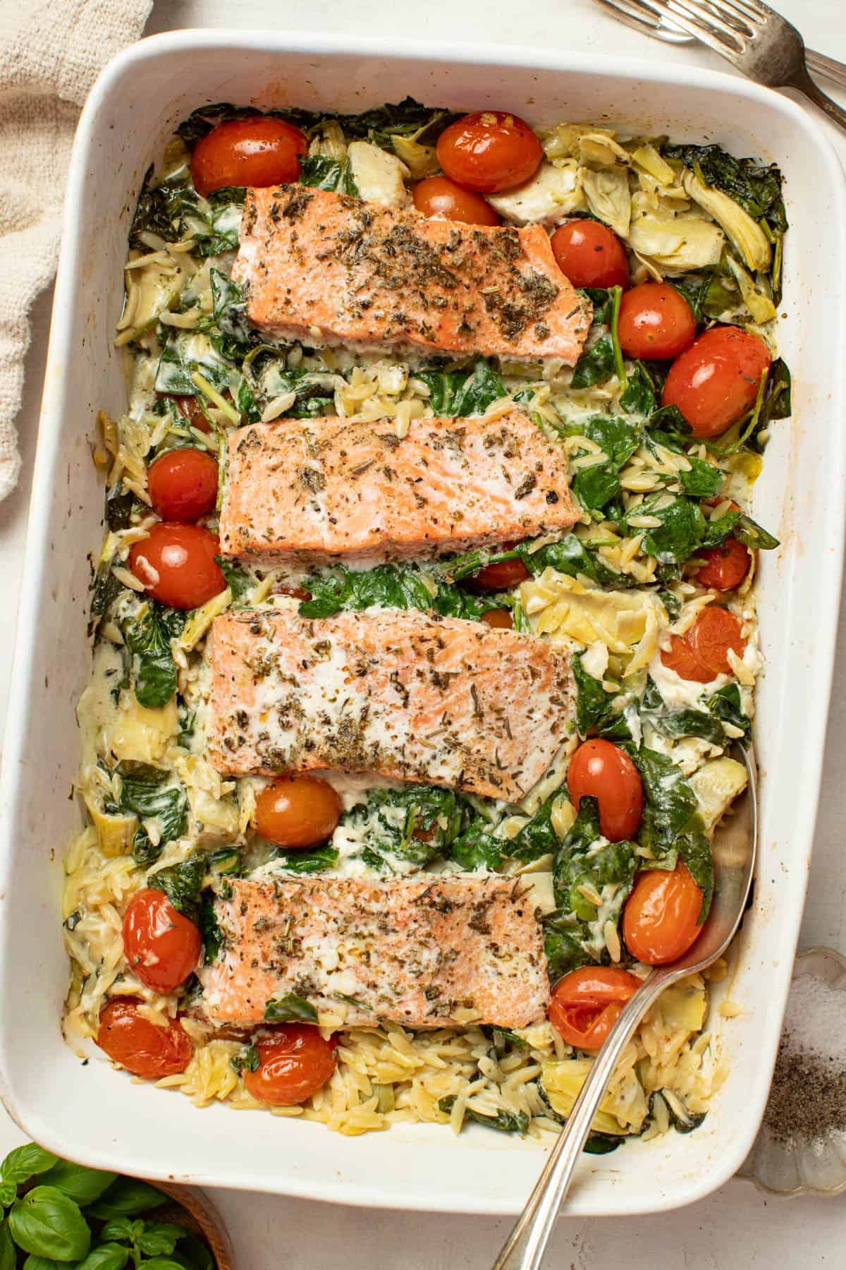 Baked salmon with orzo, tomatoes, artichokes, and spinach in a baking dish.