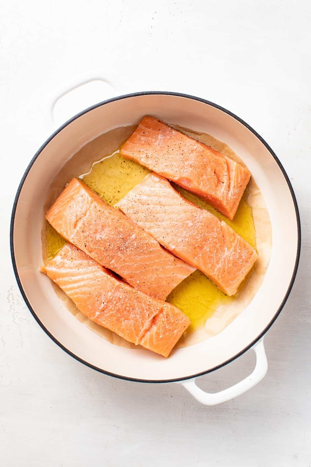 Four salmon fillets being seared in a pan.