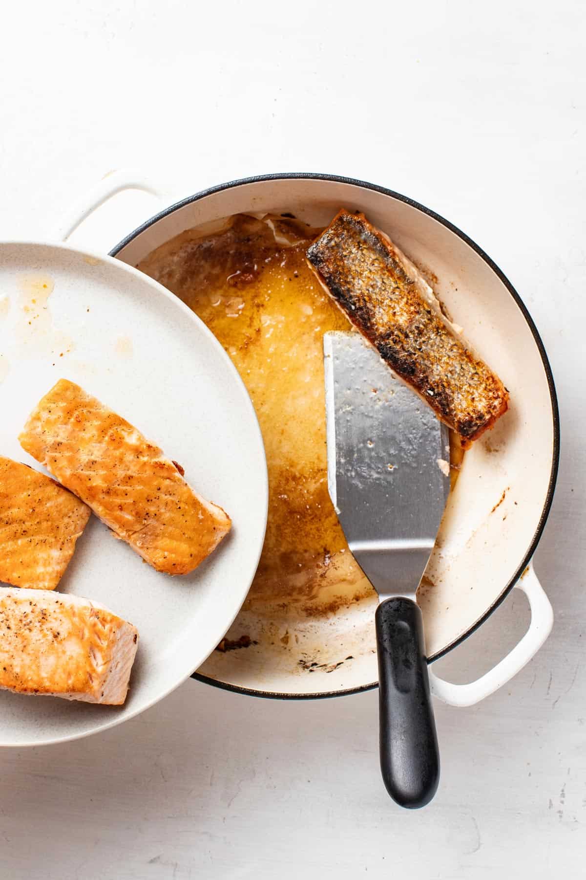 Salmon fillets being removed from a pan, golden brown after cooking.