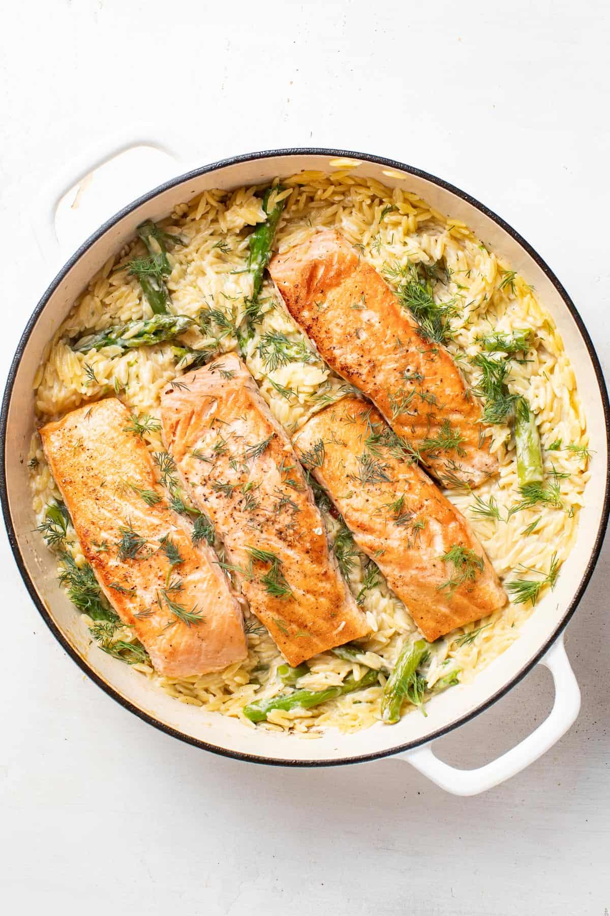 Salmon fillets nestled into the creamy asparagus and lemon orzo in the white pan.