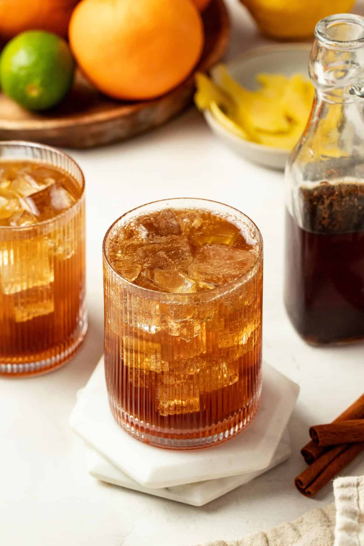 Two glasses of cola with ice on a table next to the cola syrup.