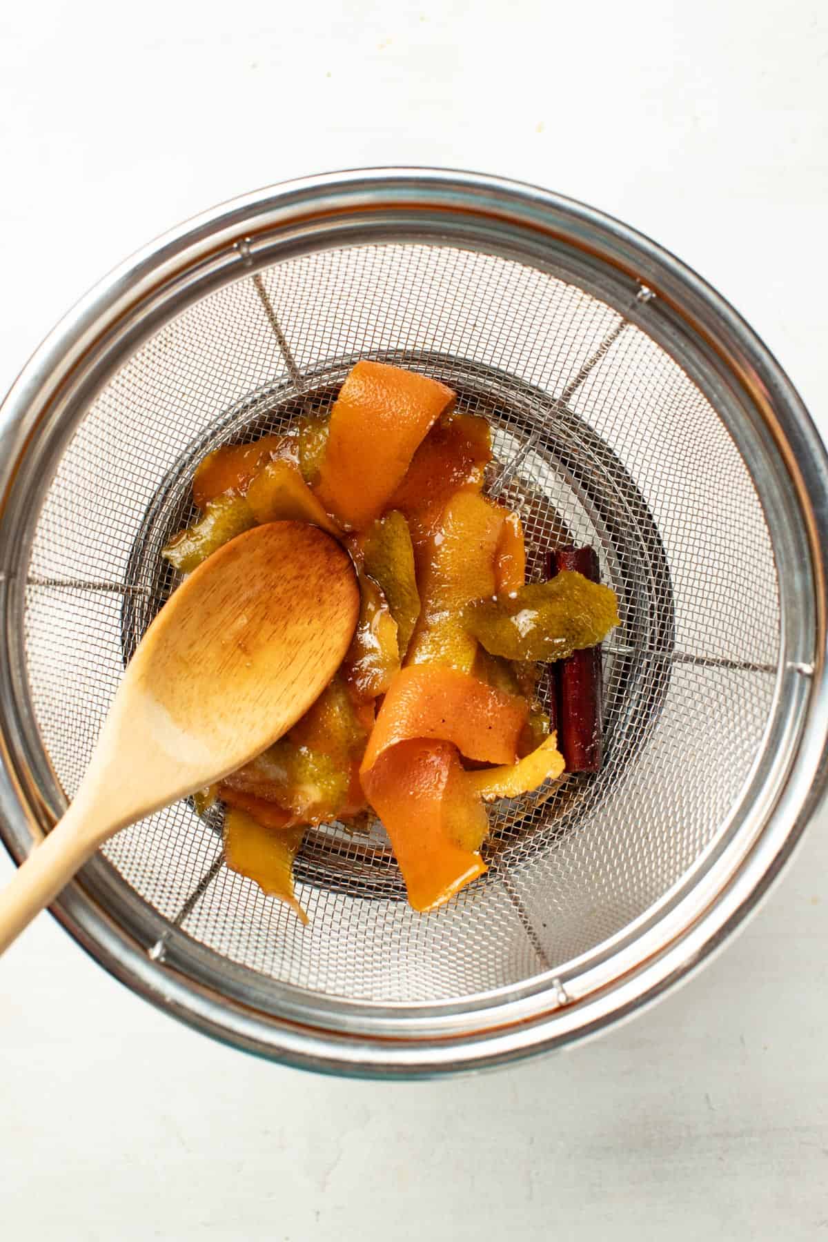 Straining the ginger and citrus peels out of the cola syrup through a fine mesh strainer.