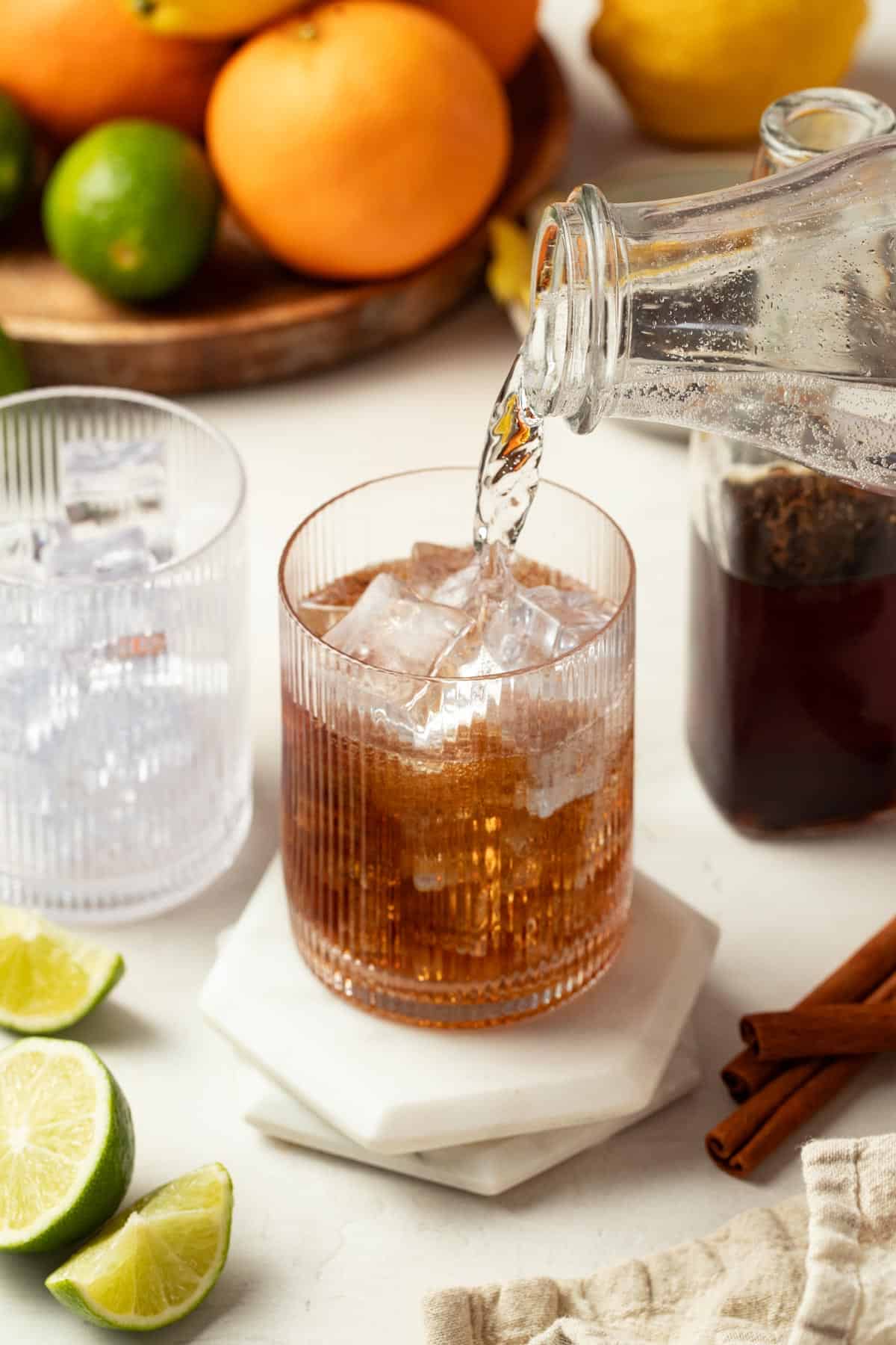 Pouring sparkling water on top of the syrup in a glass with ice.