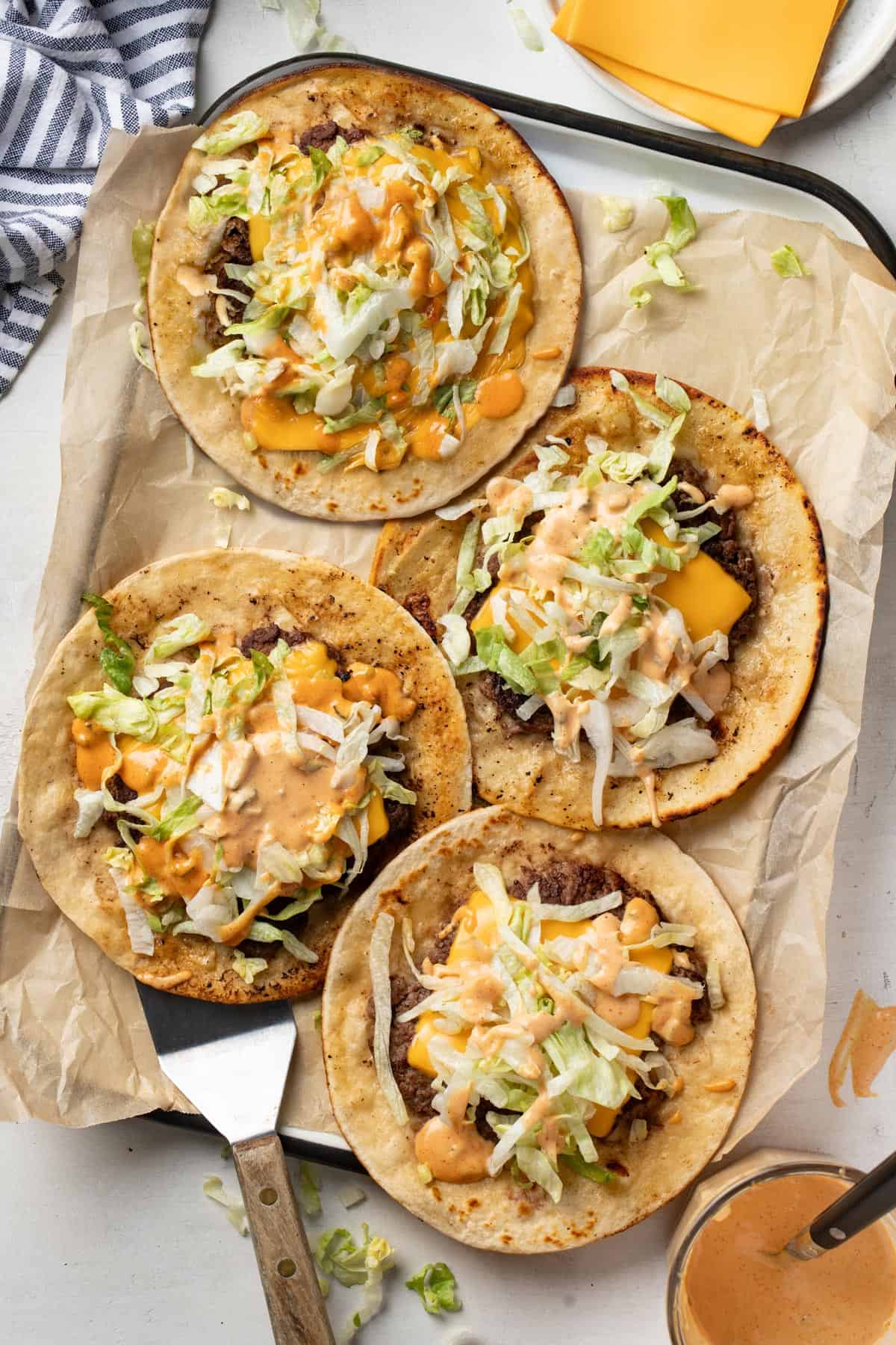 Four smash burger tacos on a tray, topped with burger sauce and shredded lettuce.