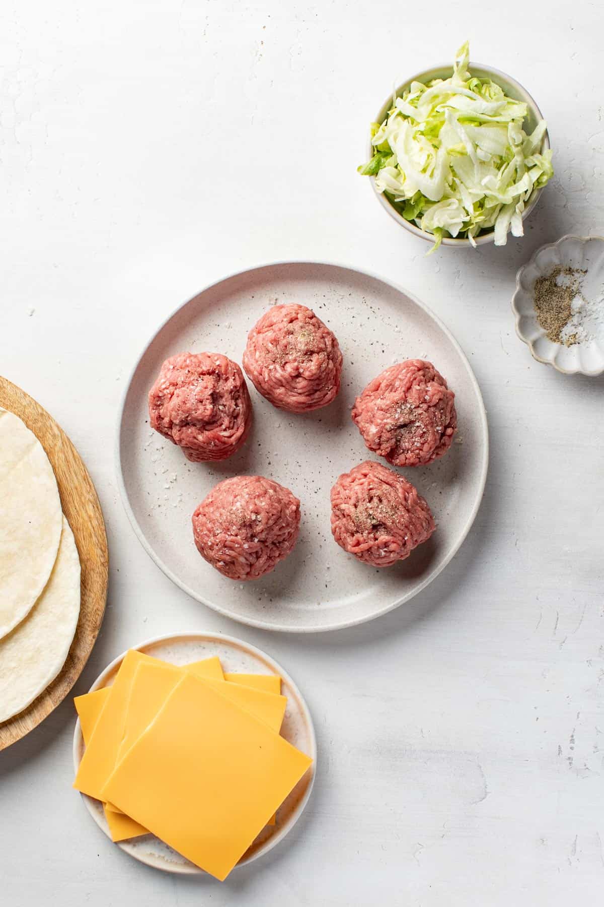 Five balls of ground beef for burgers on a plate.