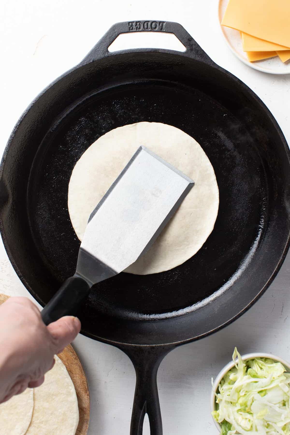 Smashing the ground beef under a tortilla with a spatula.