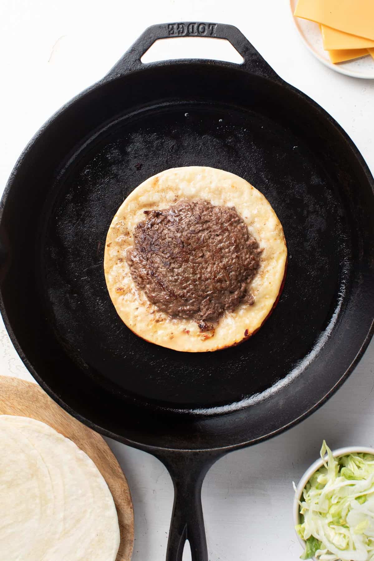 The smash burger taco after being flipped in a cast iron pan.