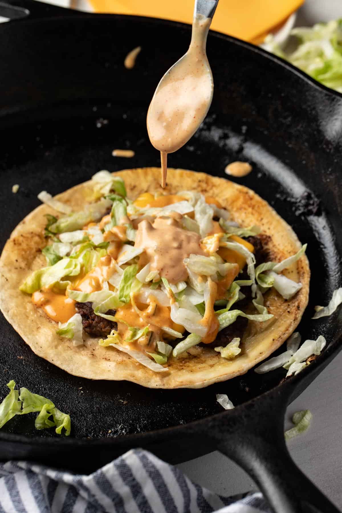 Drizzling the homemade burger sauce on top of the smashed burger taco with lettuce.