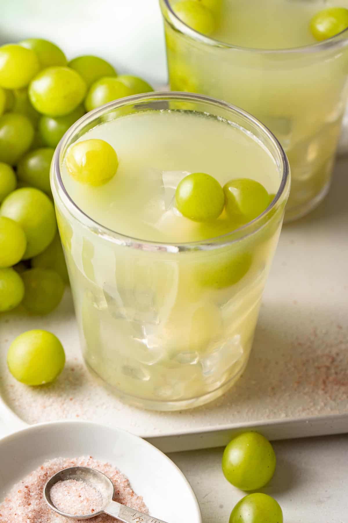 A sour grape drink on a tray next to green grapes and mineral salt.