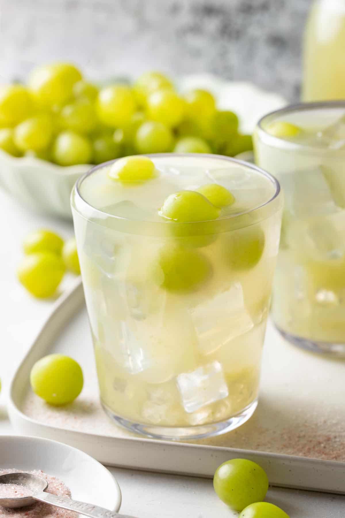 Green grape hydration drink on a tray with a bowl of green grapes in the background.