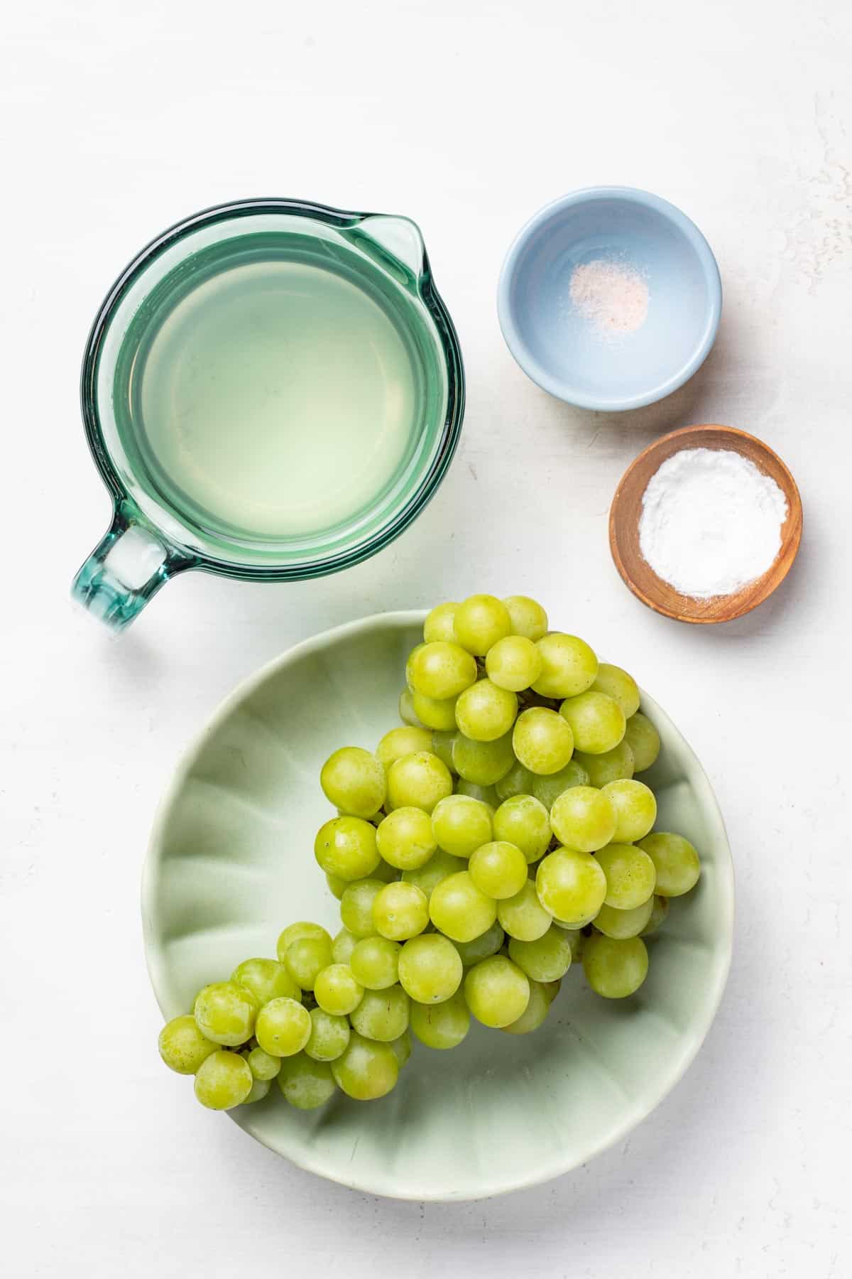 Ingredients for the grape hydration drink on a table including coconut water, salt, and green grapes.