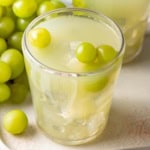 A sour grape drink with fresh green grapes on top.