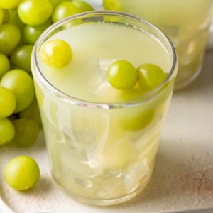 A sour grape drink with fresh green grapes on top.