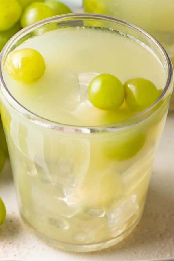 A sour grape drink with fresh green grapes on top.
