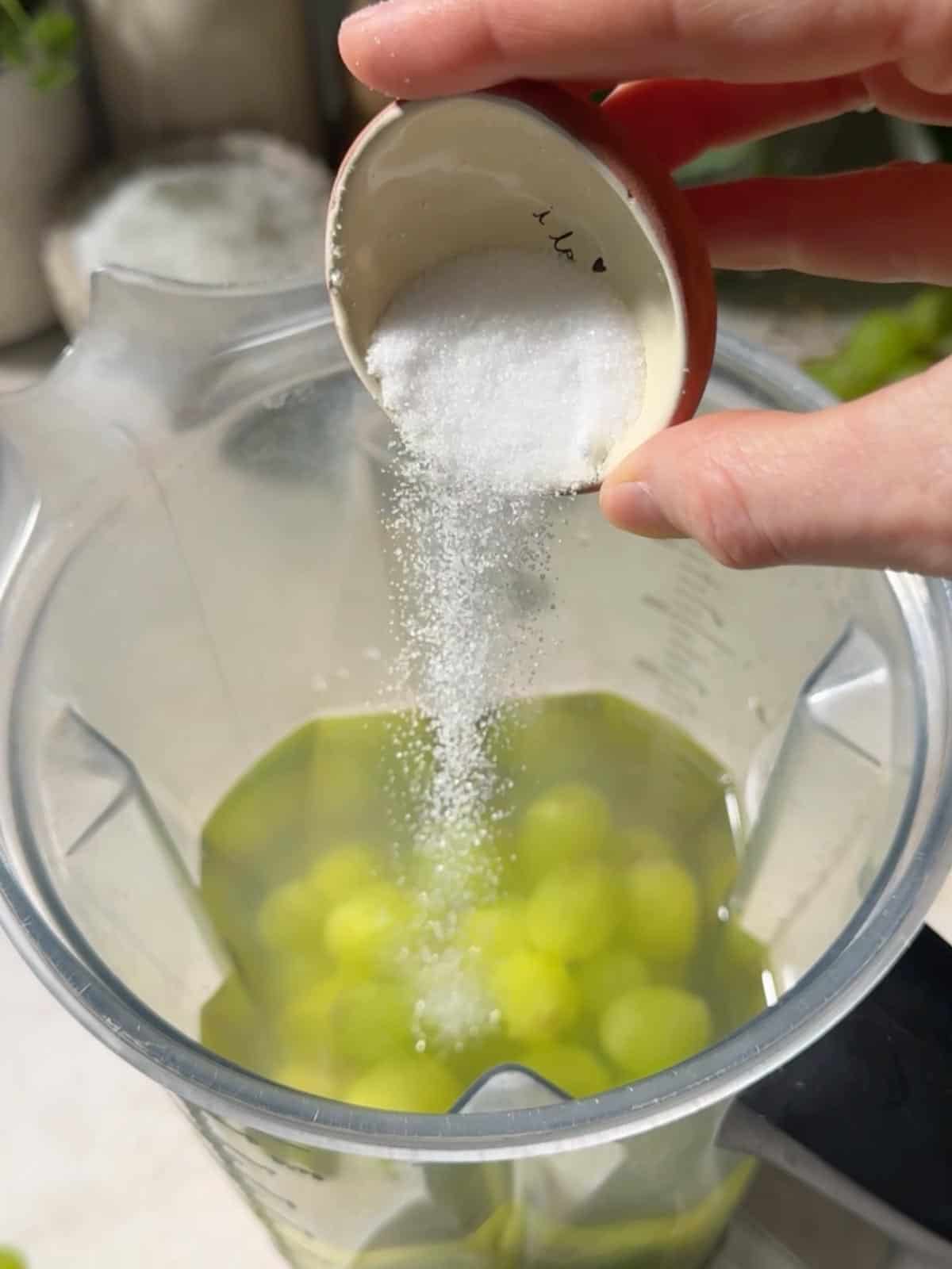 Pouring ingredients into a blender with the green grapes.