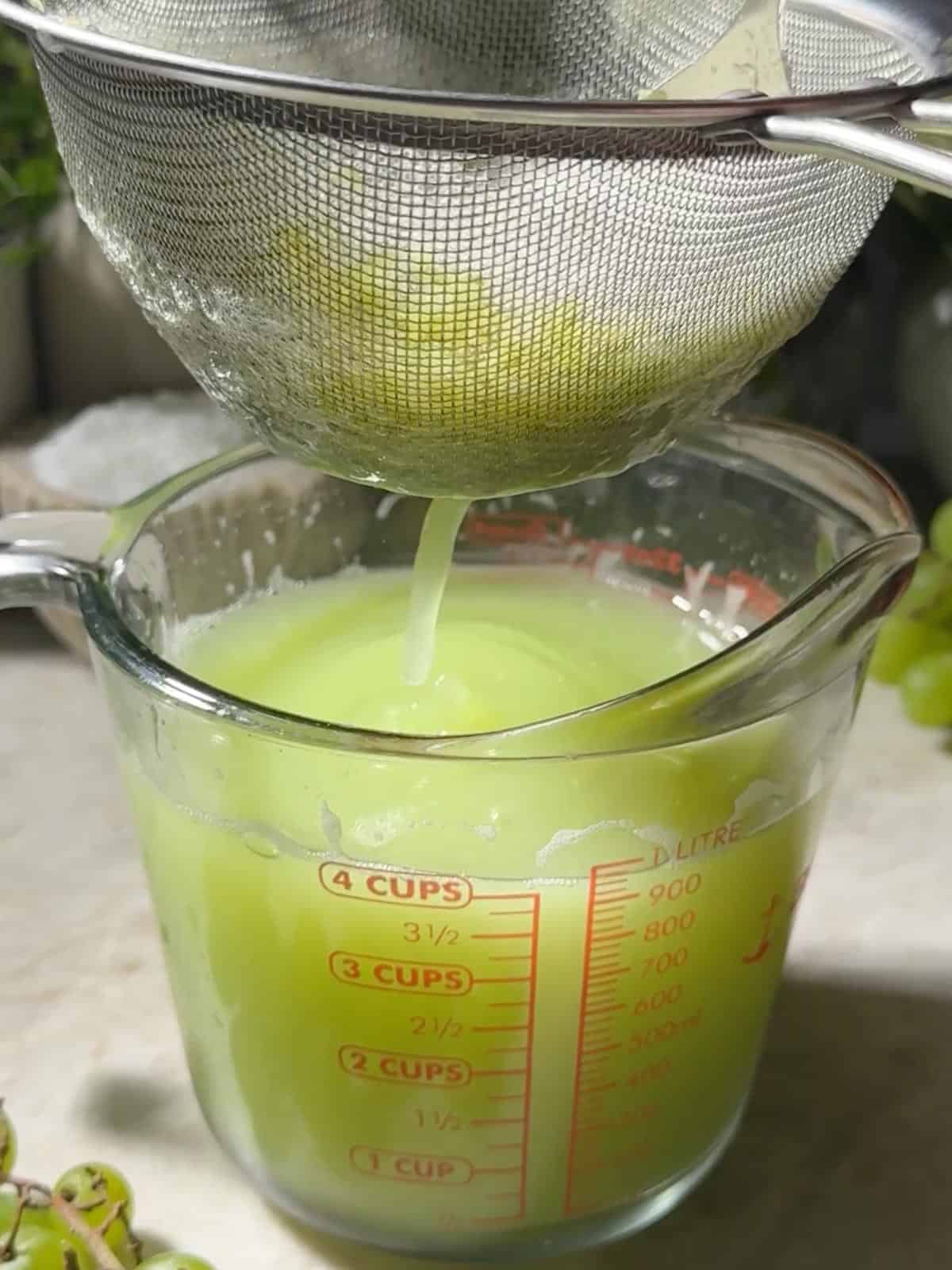 Straining the green grape juice through a fine mesh strainer into a jar.