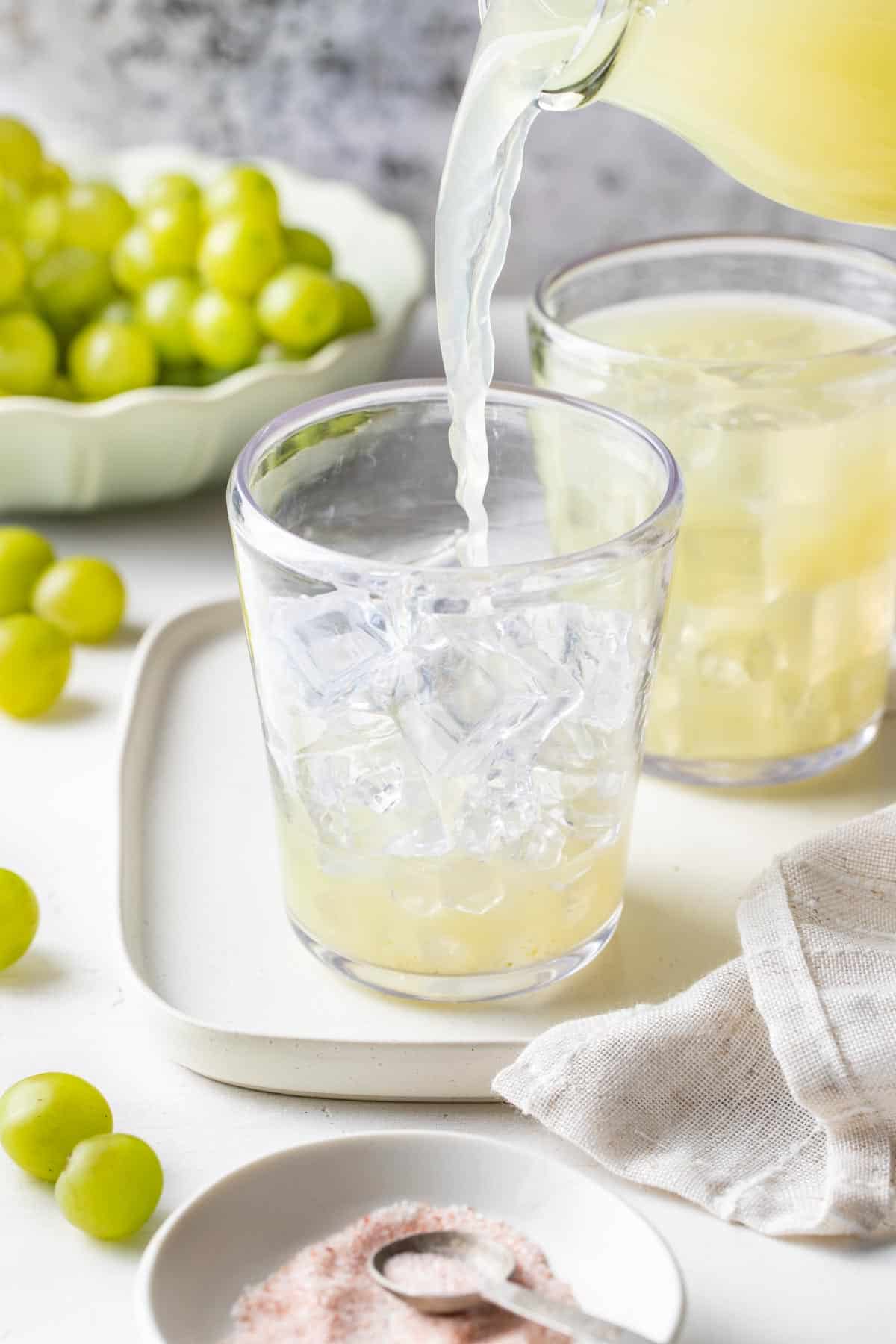 Pouring the green grape juice mixture into a glass with ice.